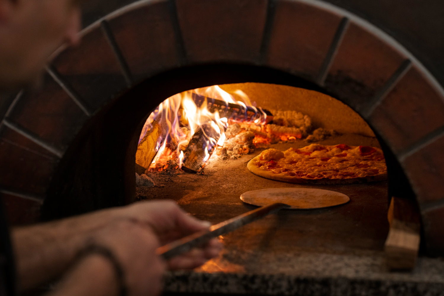 Pizza being placed insidewood fired oven