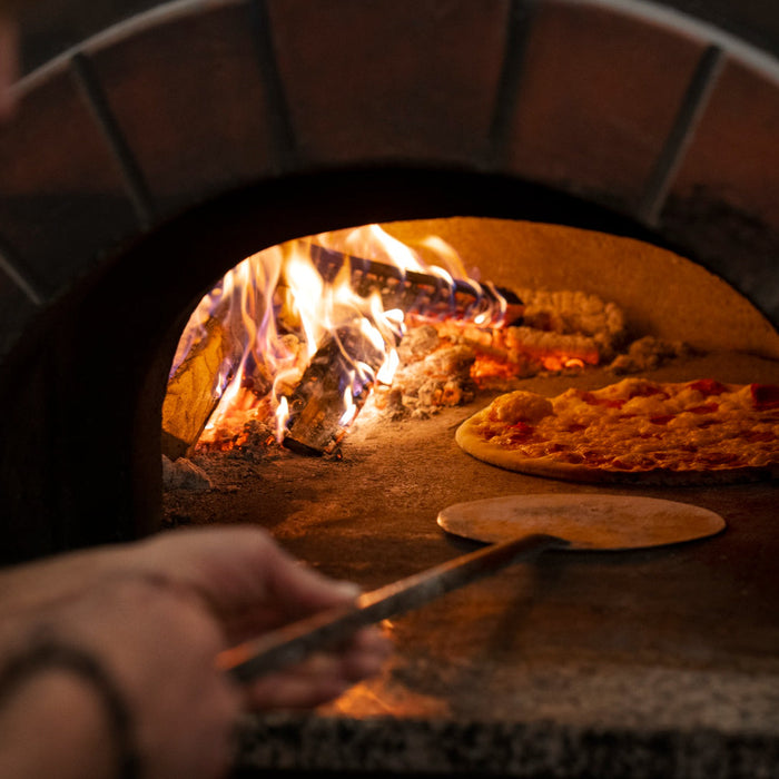 Pizza being placed insidewood fired oven
