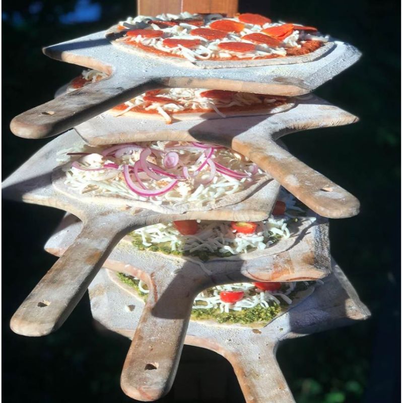 A pizza being placed onto a wooden pizza peel for transfer to a pizza oven
